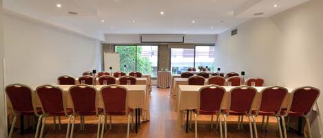 A conference room with multiple tables and chairs, large windows, and a view of greenery outside.