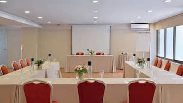 Un salón de conferencias con una mesa larga, sillas rojas y una pantalla de proyector.