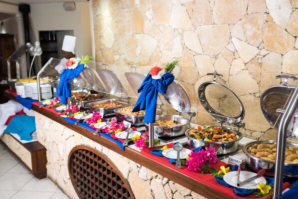Ein reichhaltiges Buffet mit verschiedenen Speisen vor einer Wand aus Naturstein.