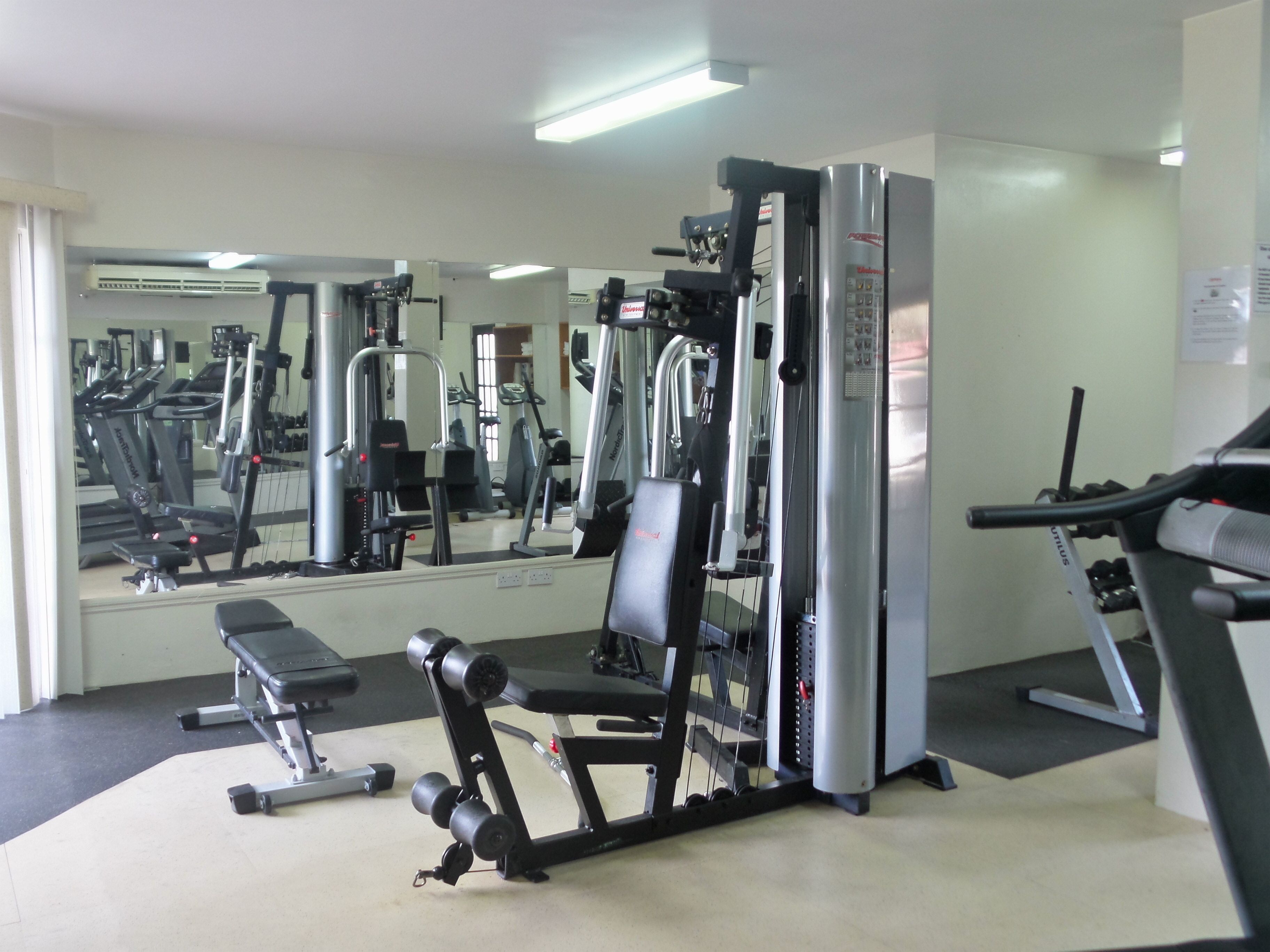 A gym with exercise equipment, a bench, and a mirrored wall.
