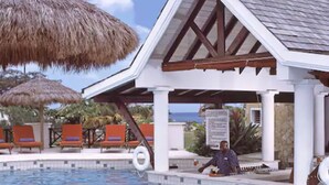 A pool area with a thatched umbrella, lounge chairs, and a small pavilion with a tiled roof. - Coyaba Beach Resort (St. George's)