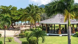 A gazebo with a tiled roof surrounded by palm trees and a beach area with lounge chairs. - Coyaba Beach Resort (St. George's)