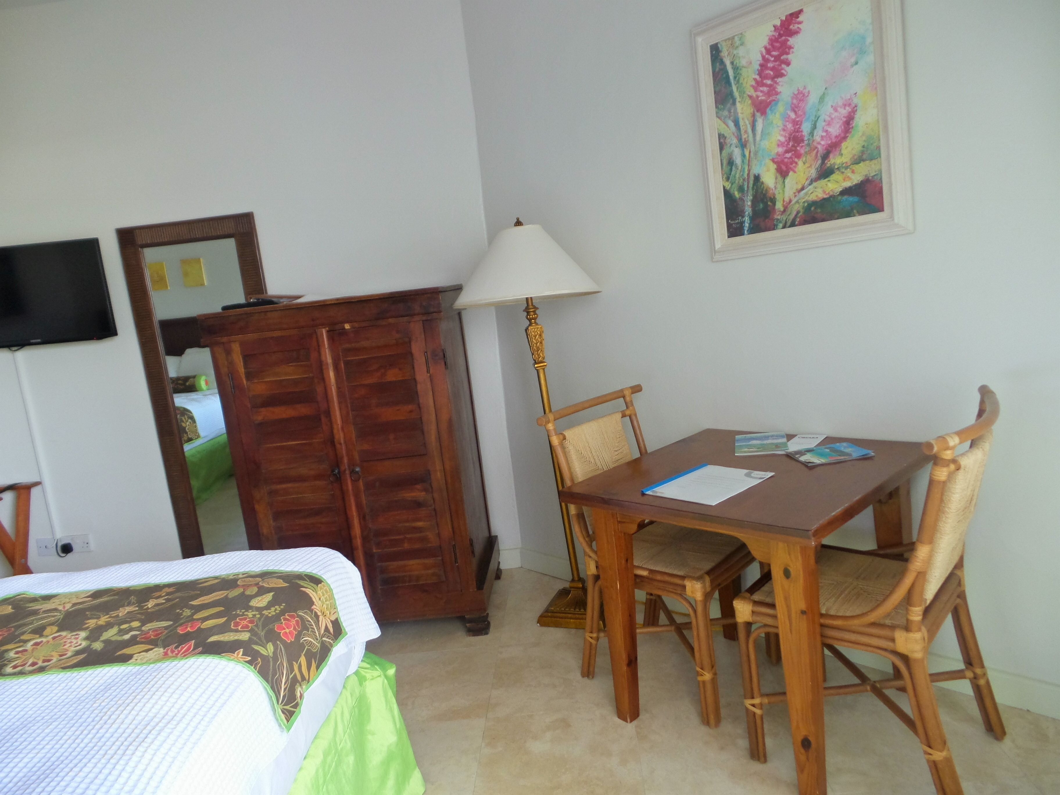 Une pièce comprenant un lit, une armoire en bois, une table à manger avec des chaises, une lampe et un tableau accroché au mur.