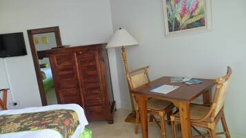 A room with a bed, a wooden wardrobe, a dining table with chairs, a lamp, and a painting on the wall.