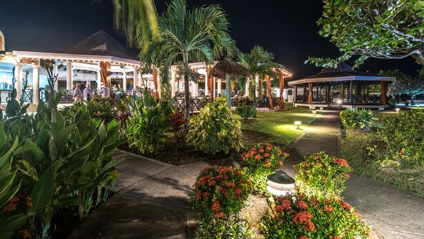 A well-lit outdoor area with a covered seating area, palm trees, and a pathway. - Coyaba Beach Resort (St. George's)