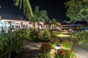 A well-lit outdoor area with a covered seating area, palm trees, and a pathway. - Coyaba Beach Resort (St. George's)