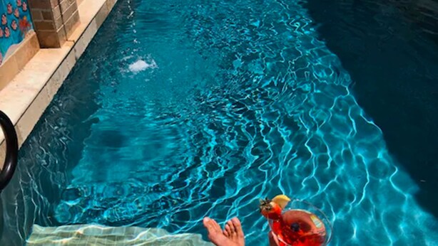 A pool with clear blue water and a person holding a drink.