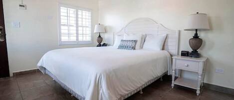 A bedroom with a large bed, two bedside tables with lamps, a window, and a door.