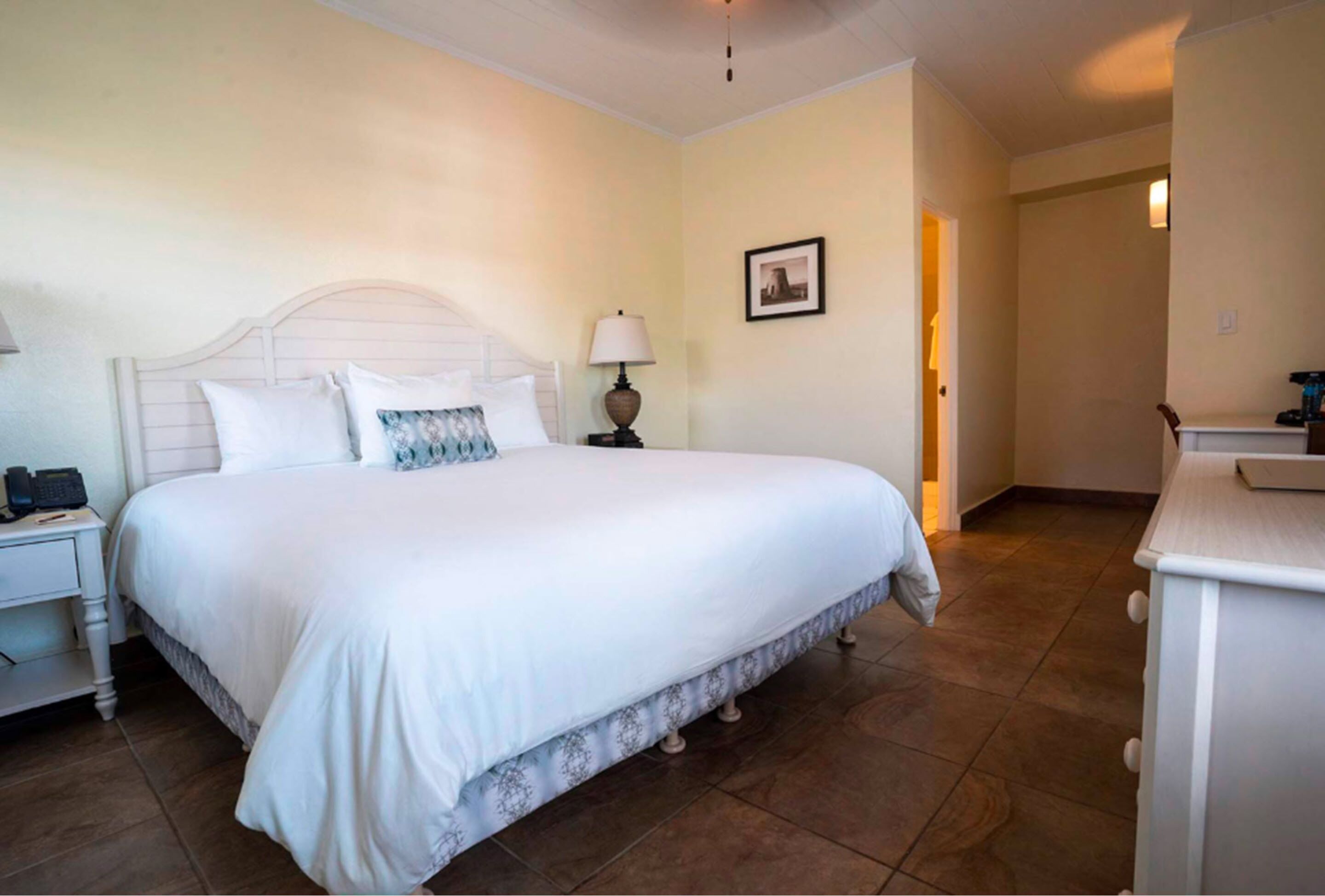 A neatly arranged bedroom with a large bed, a bedside table with a lamp, and a small desk with a chair.