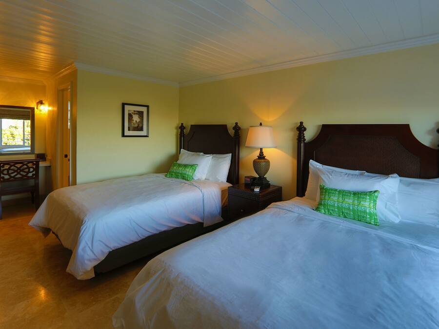 A hotel room with two beds, a nightstand with a lamp, a wooden chair, and a framed picture on the wall.