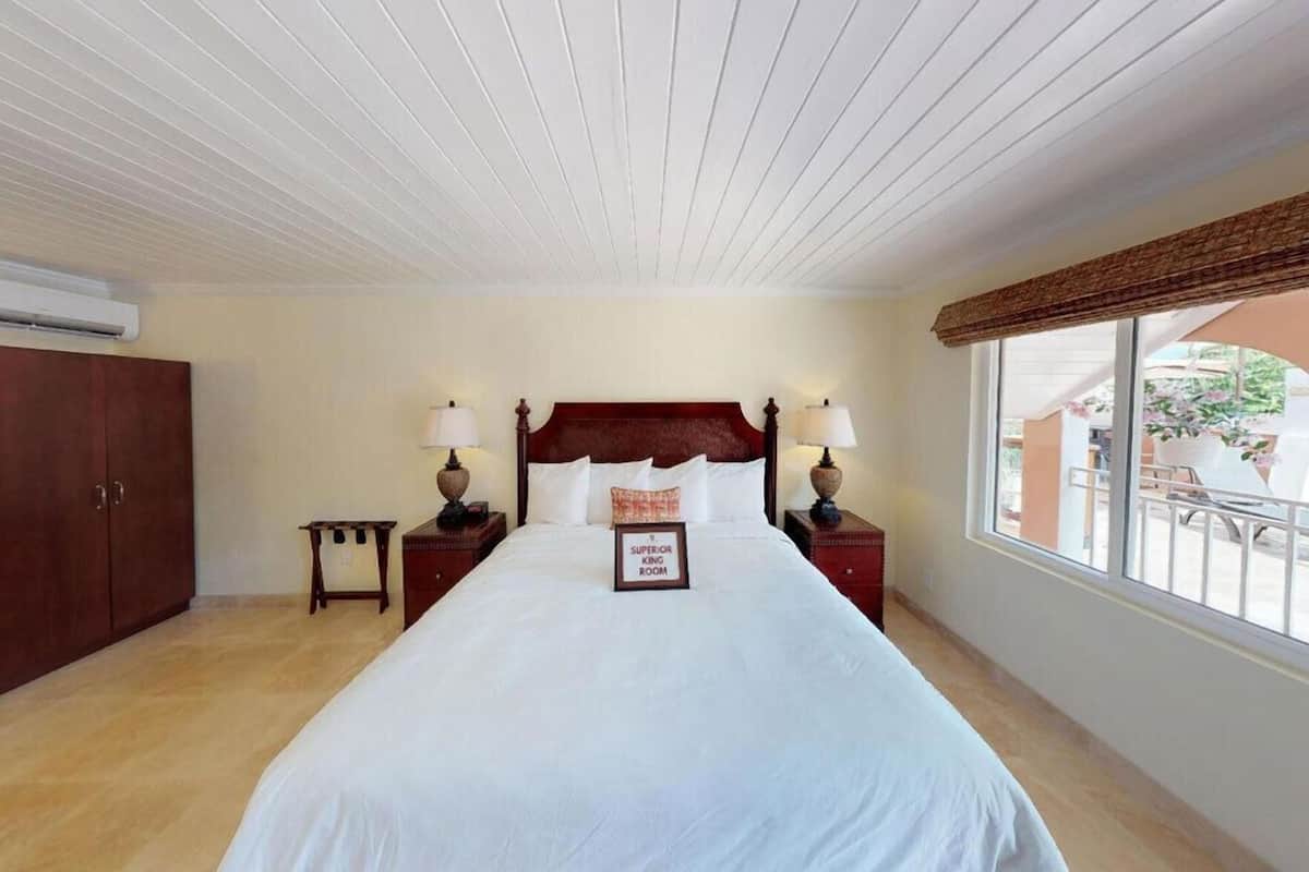 A bedroom with a large bed, two bedside tables with lamps, a wardrobe, and a window with a view.