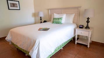 A neatly made bed with white bedding and a green accent pillow, a bedside table with a lamp, and a framed picture on the wall.