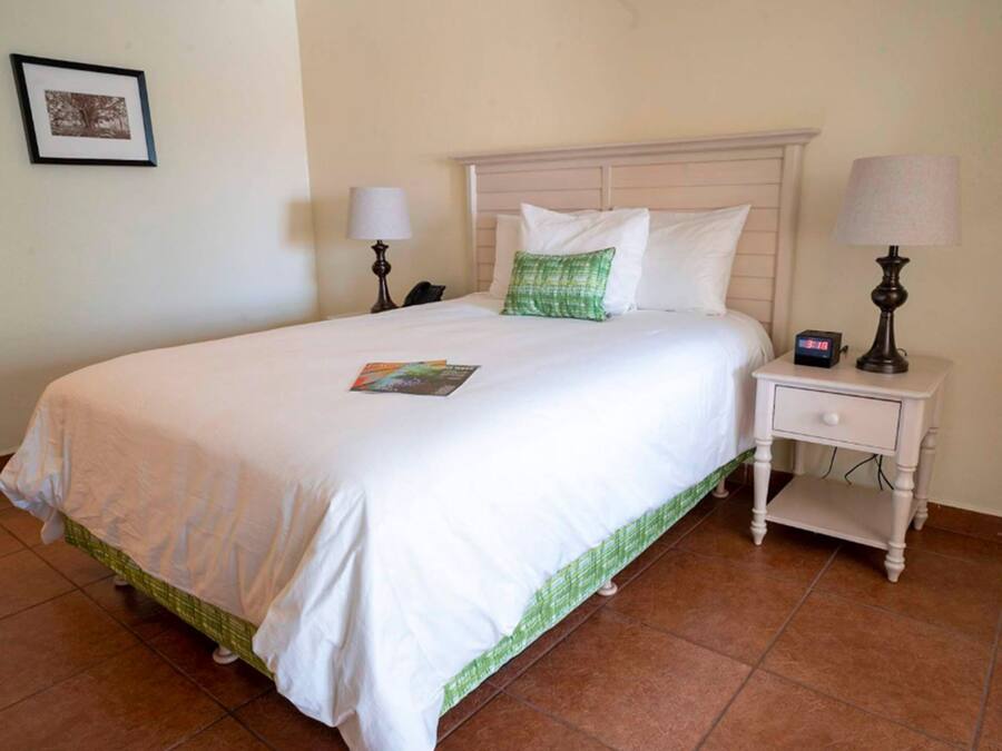 A neatly made bed with white bedding and a green accent pillow, a bedside table with a lamp, and a framed picture on the wall.