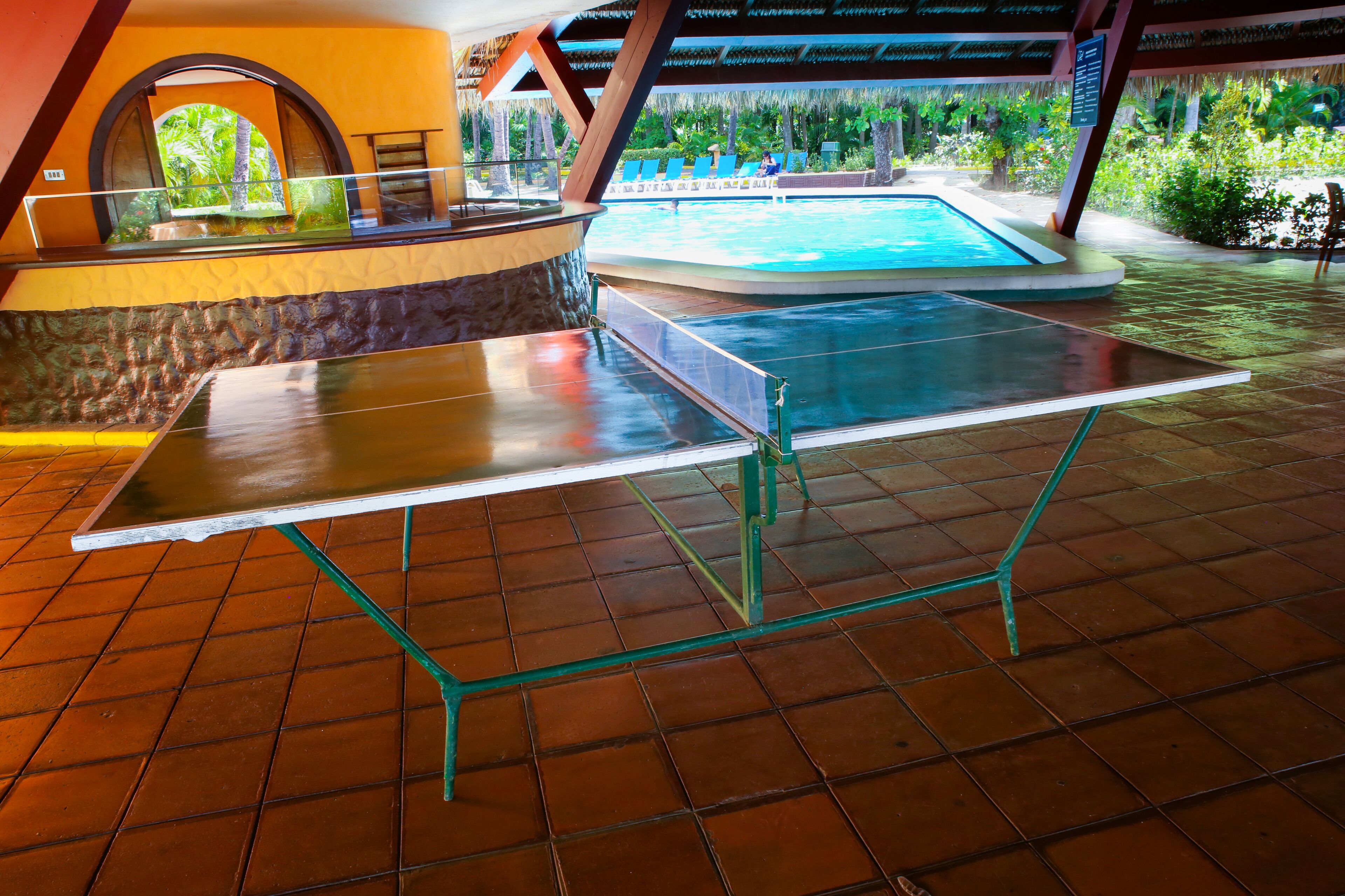 A ping pong table in a covered area with a pool in the background.