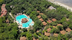 Vista aérea de un resort con piscina central, rodeado de exuberante vegetación y acceso a la playa.