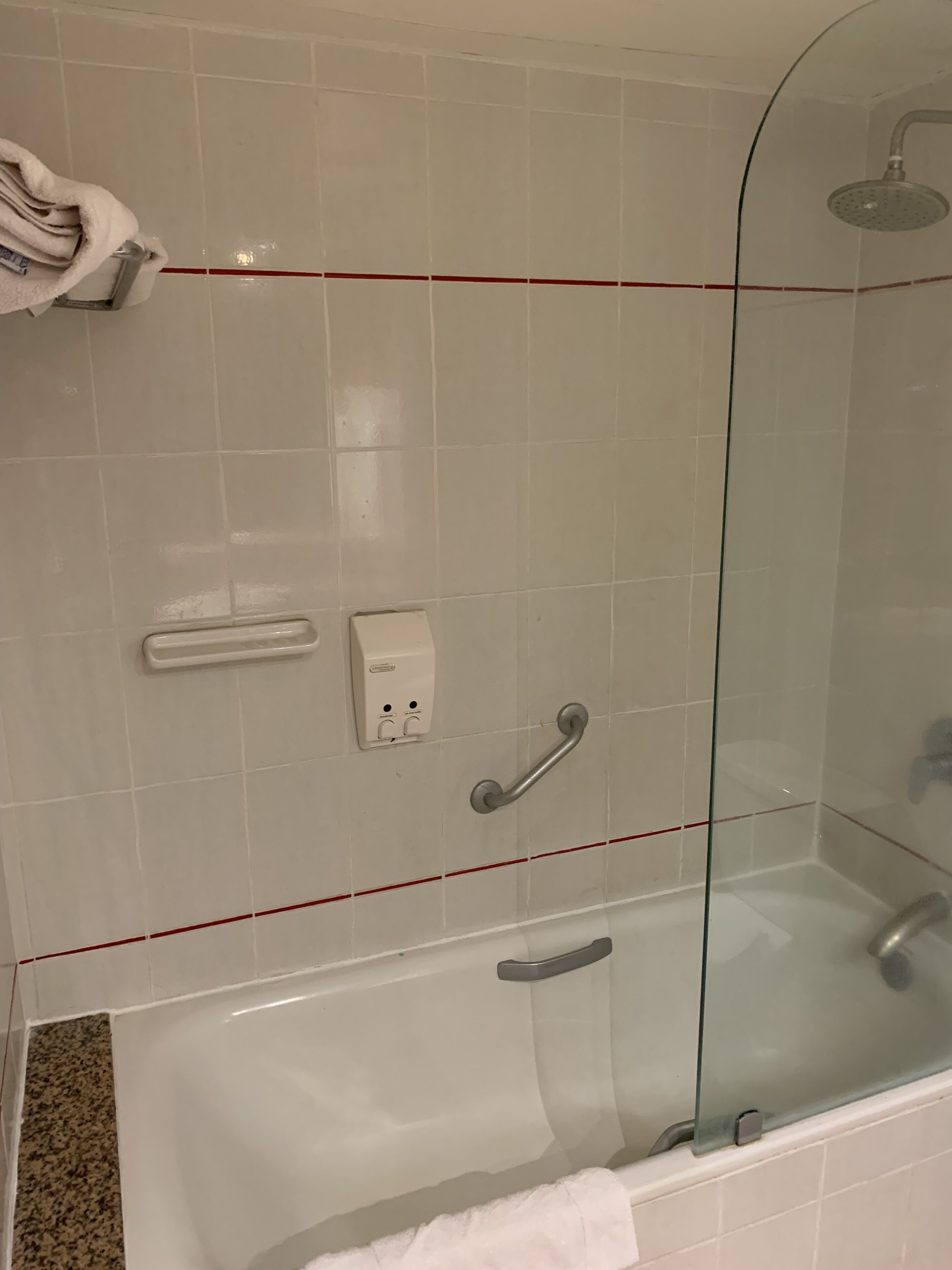 A modern bathroom with a glass-enclosed shower, a white bathtub, and a hand dryer.