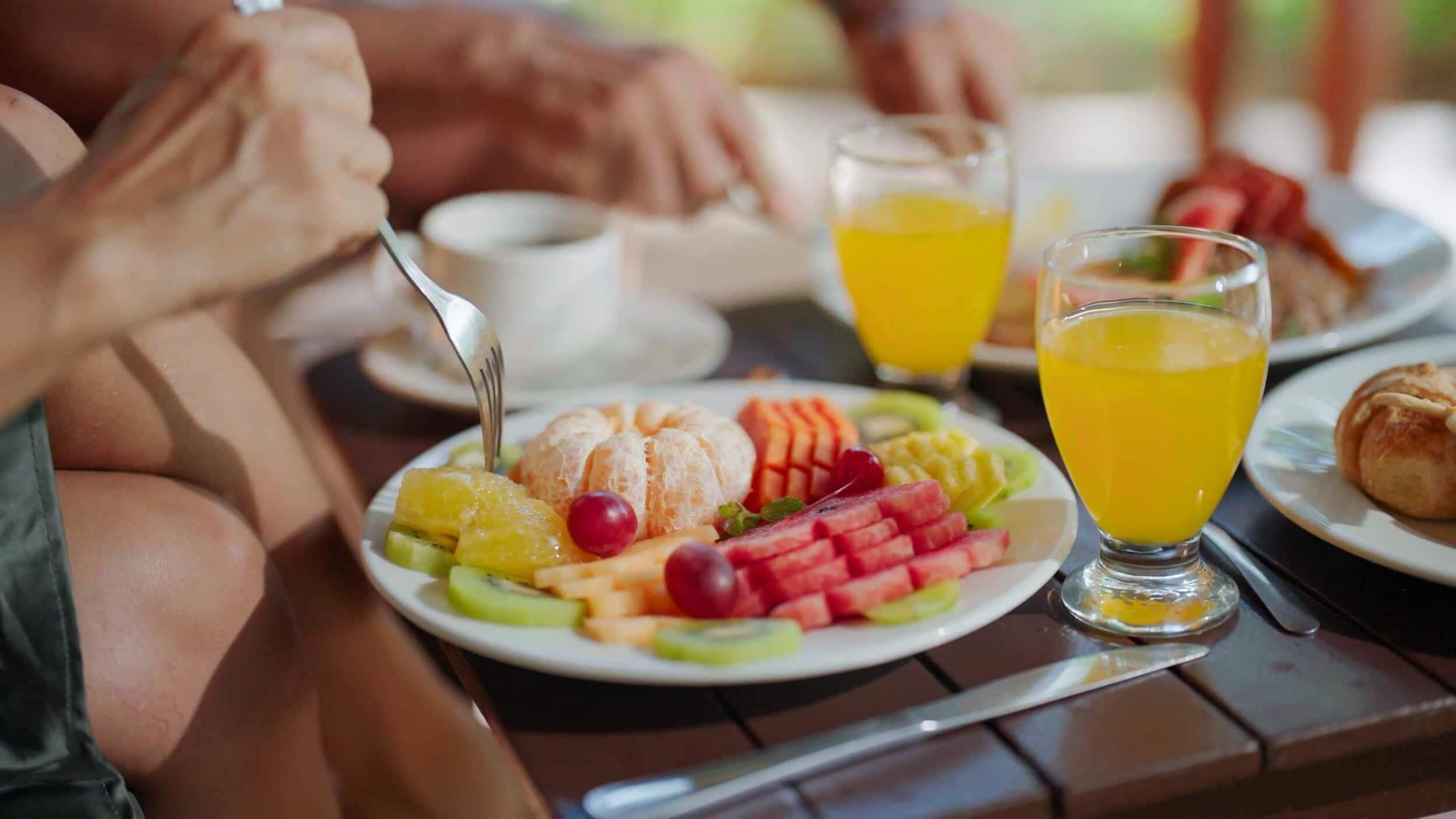 Een ontbijtje met een fruitschaal, een glas sinaasappelsap en een croissant.