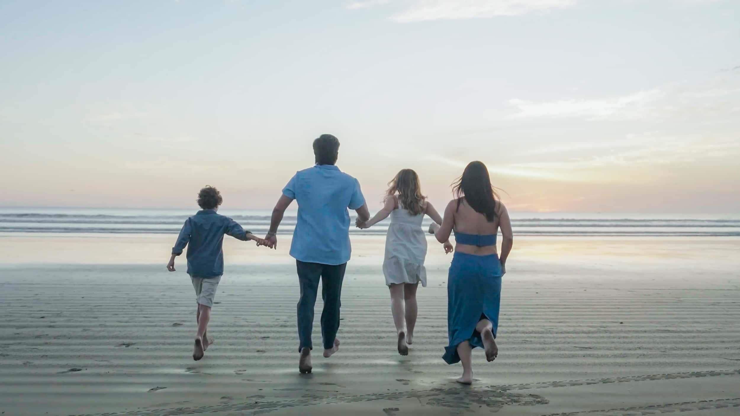 A family walking on a beach with a calm sea and a clear sky in the background.