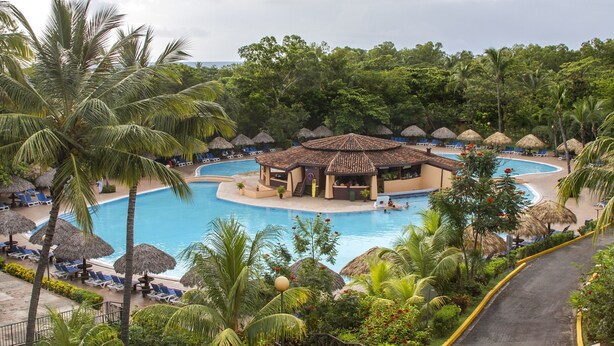 Un resort con piscina central, sillas de descanso y construcciones de techo de paja.