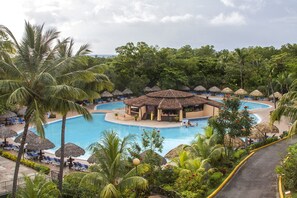 Un resort con piscina central, sillas de descanso y construcciones de techo de paja.