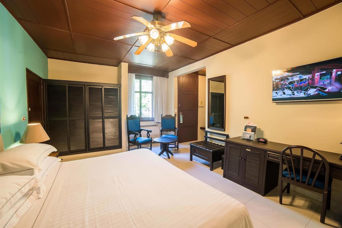 A hotel room with a bed, a desk, a chair, a television, and a ceiling fan.