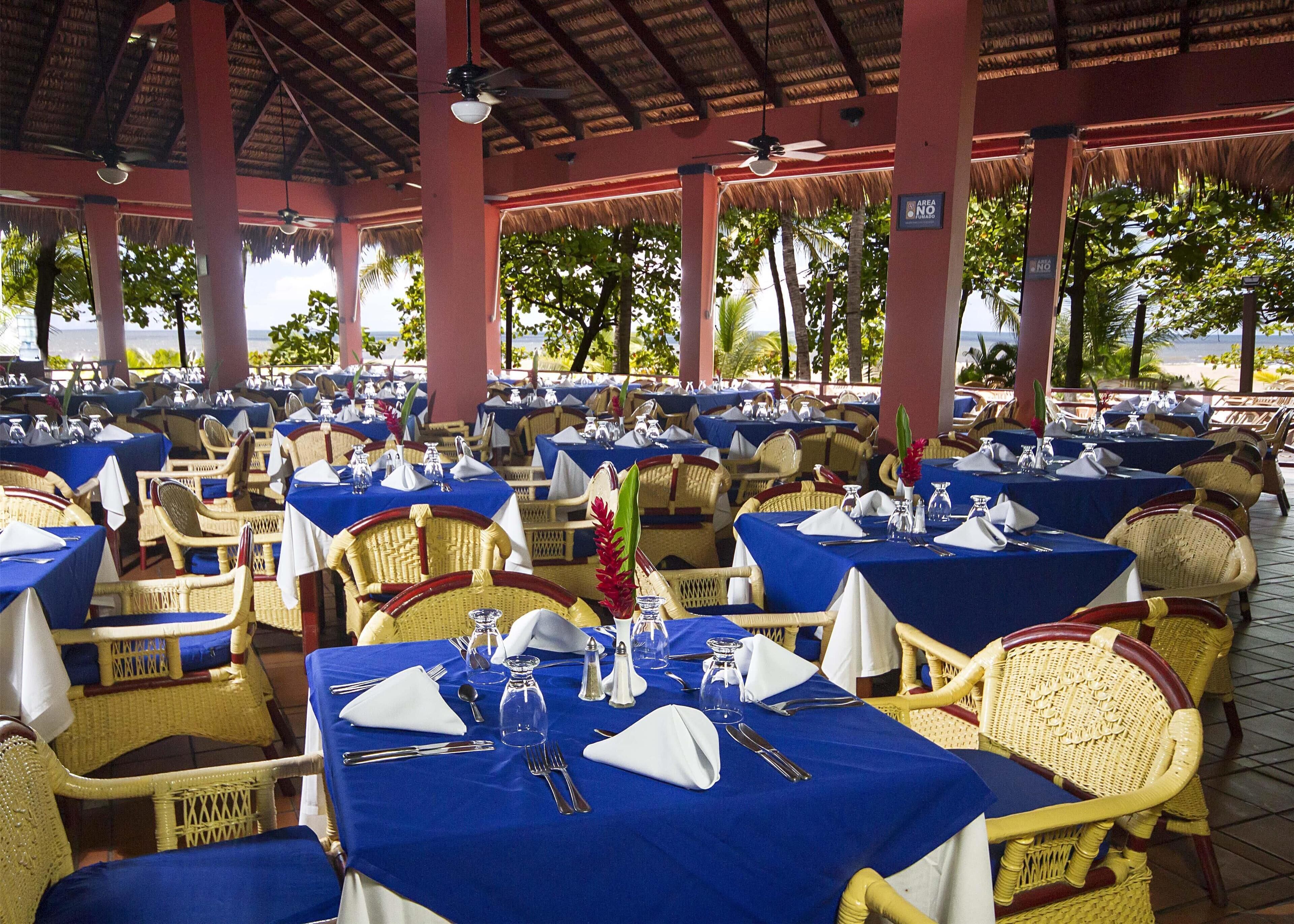 A restaurant with tables set for dining, covered by a roof, and overlooking a scenic view.