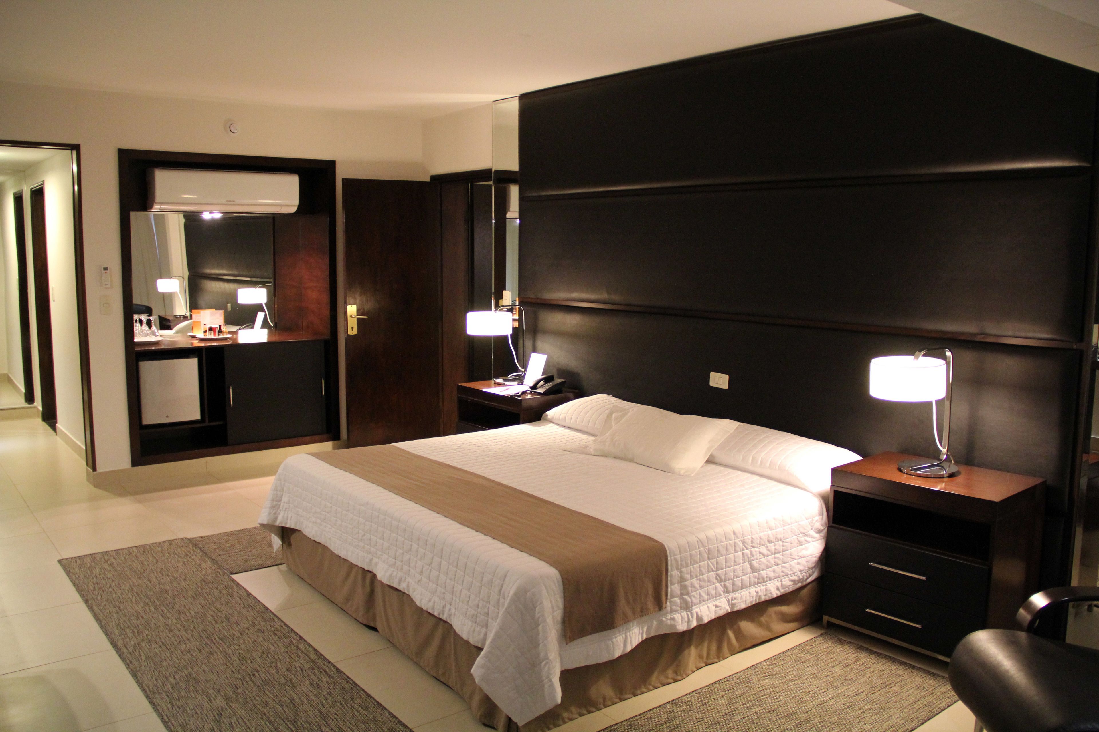 A hotel room with a large bed, bedside tables, a mirror, and a wardrobe.