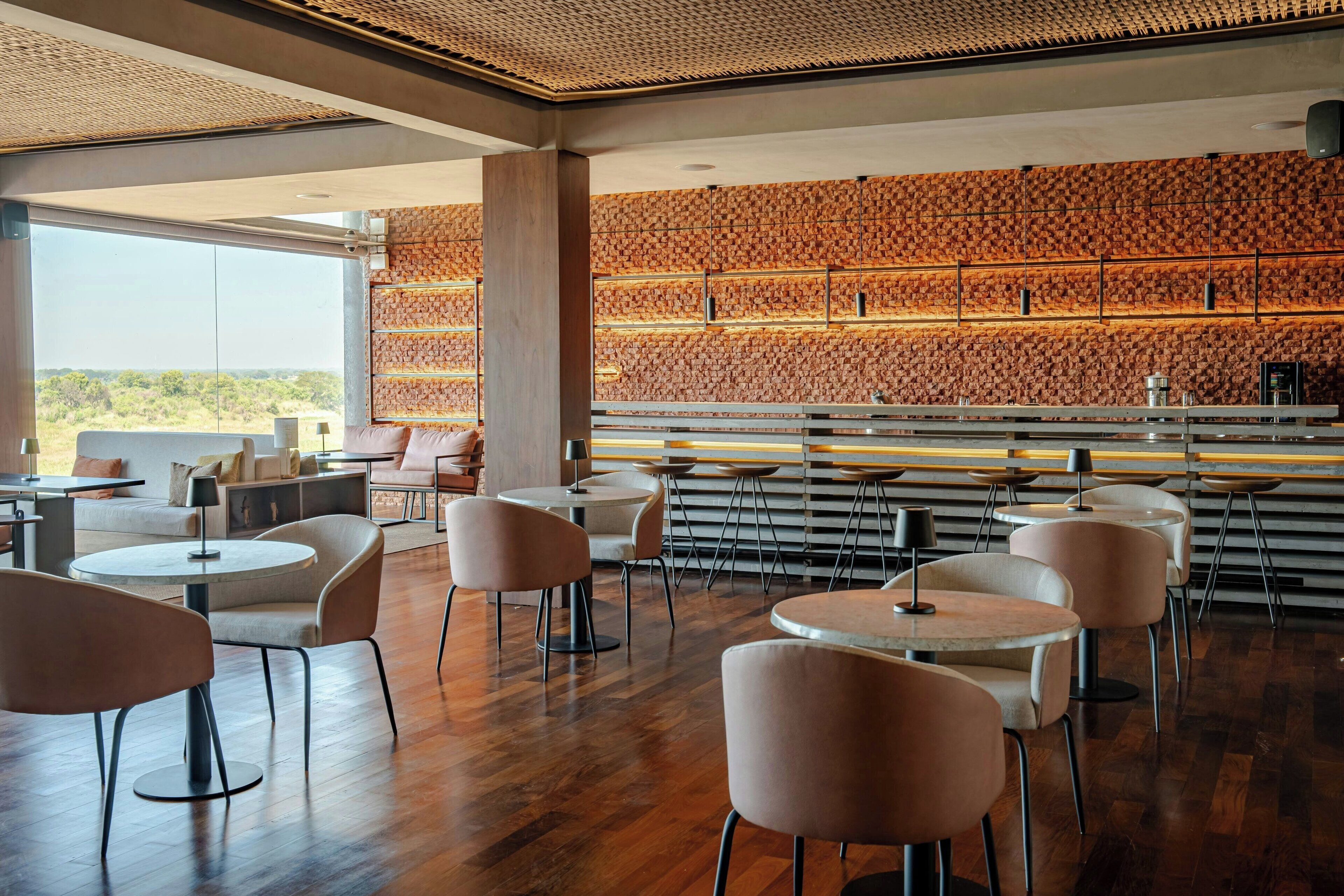 Restaurante moderno com mesas e cadeiras redondas, parede de madeira com design estampado e vista para o exterior.