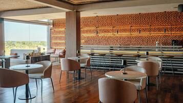 Restaurante moderno com mesas e cadeiras redondas, parede de madeira com design estampado e vista para o exterior.