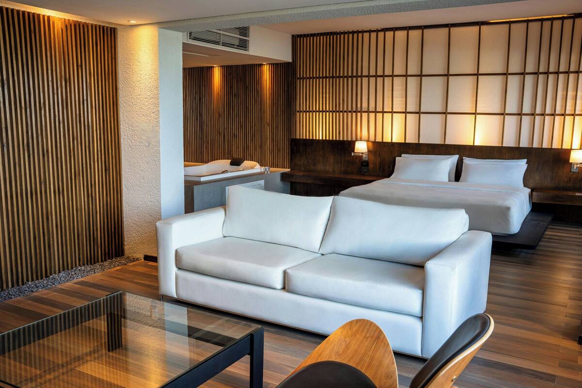 Habitación de hotel con diseño moderno, que incluye un sofá, una cama, una mesita de noche y una pared con listones de madera verticales.