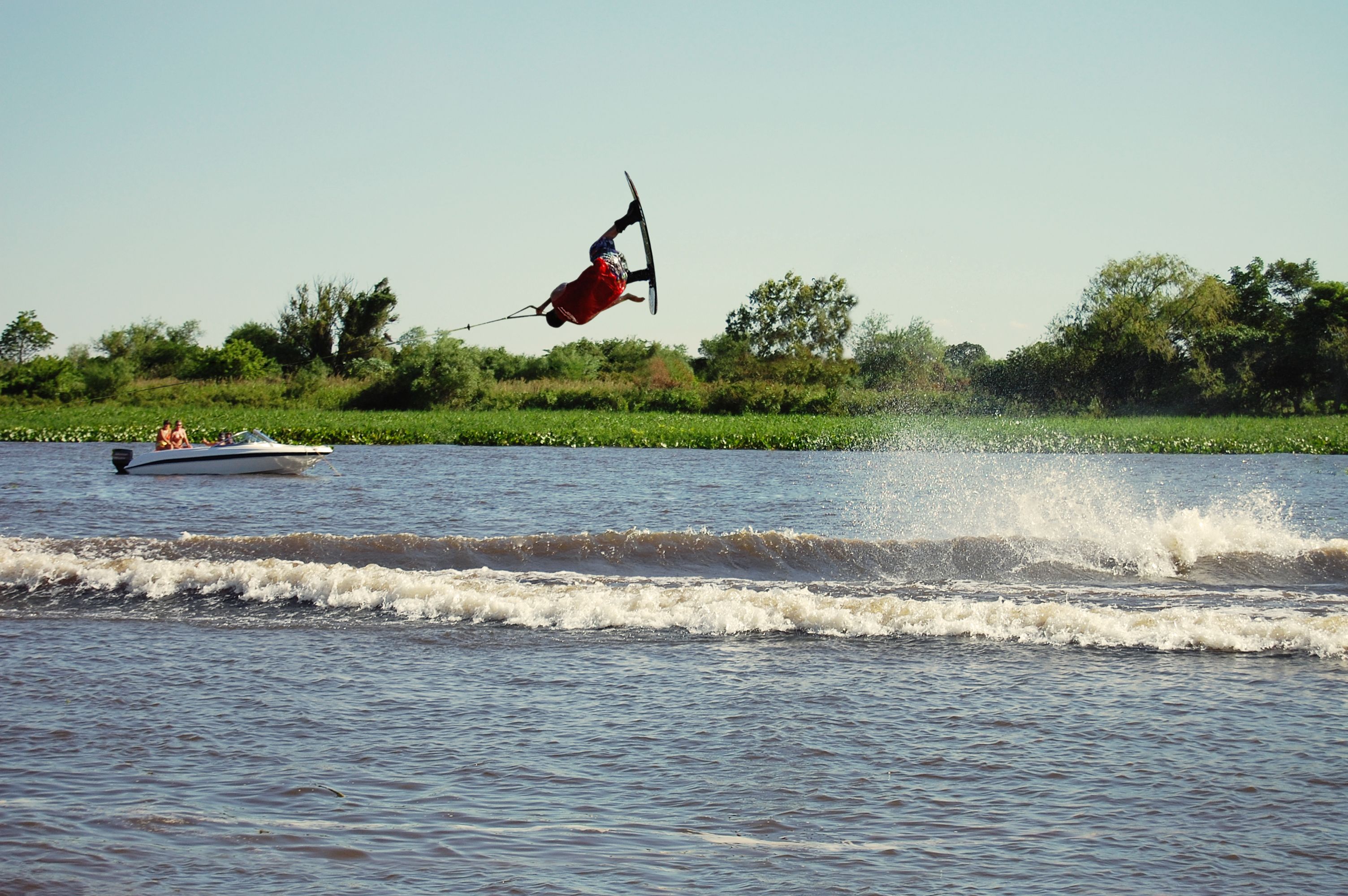 Una persona practicando wakeboard sobre el agua, con un barco al fondo.