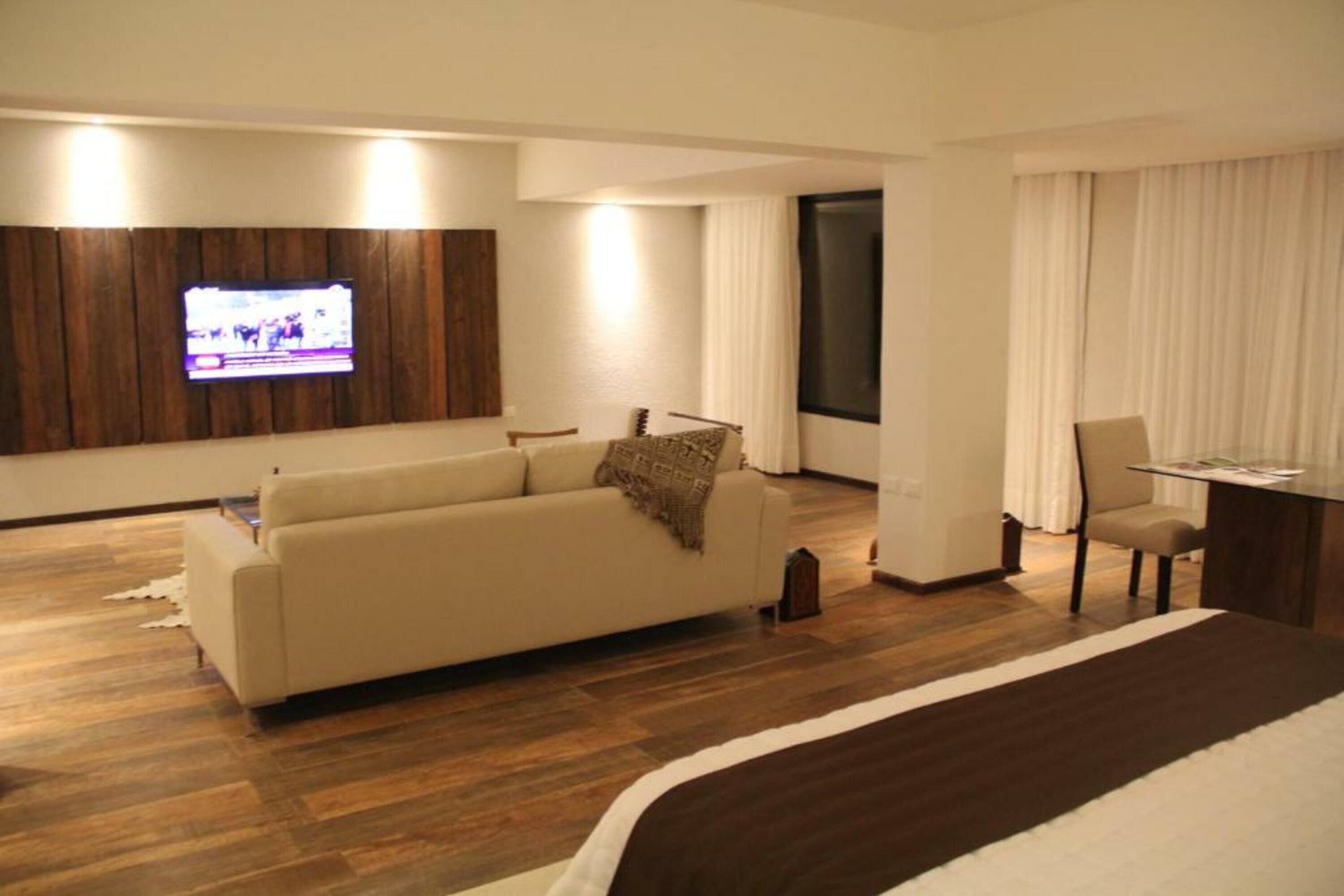 Une chambre d’hôtel moderne avec un grand lit, un canapé, un téléviseur fixé au mur, un bureau et une fenêtre avec des rideaux.
