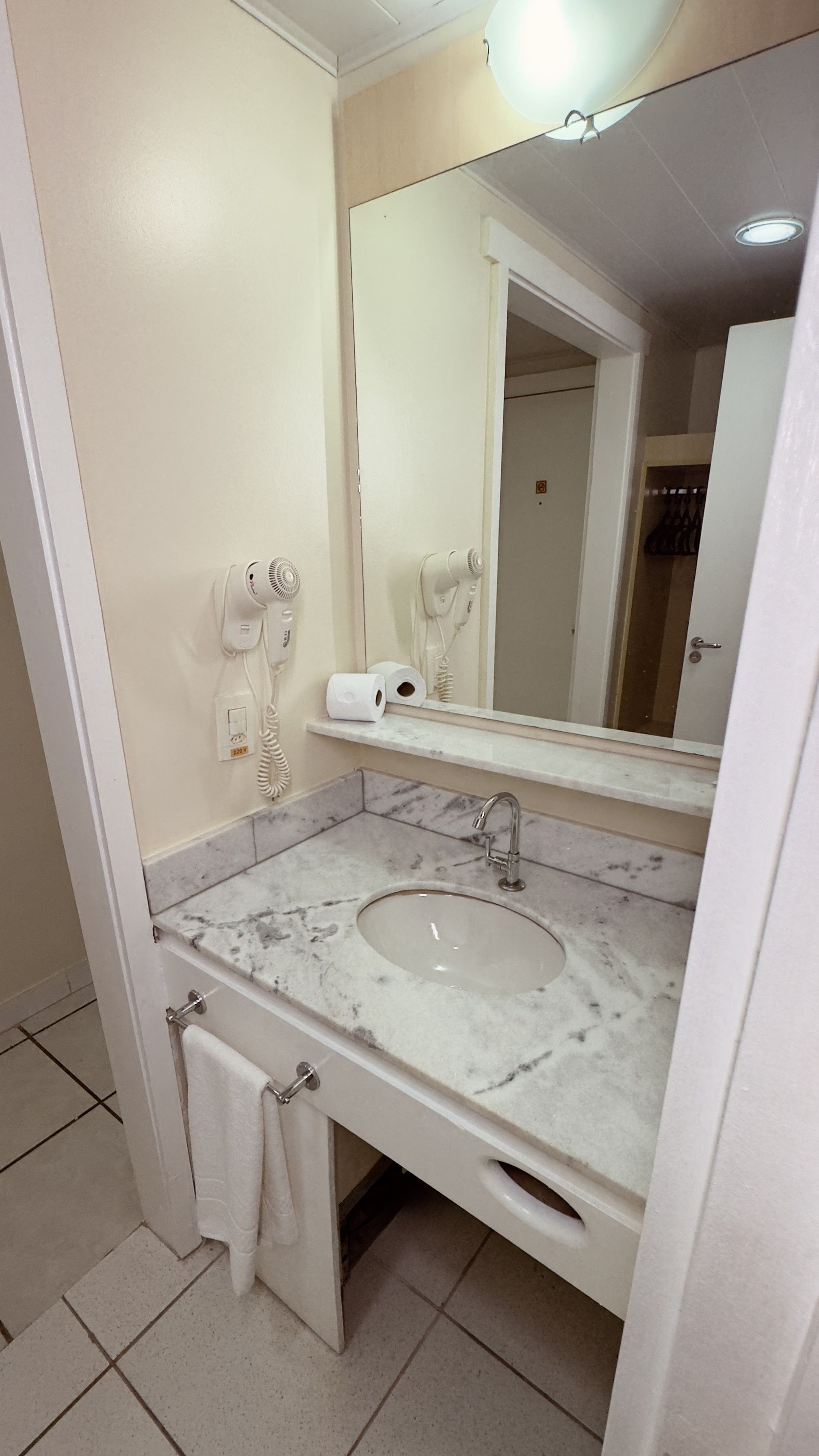 Une salle de bain avec un lavabo en marbre, un miroir, un porte-serviettes et un sèche-cheveux.