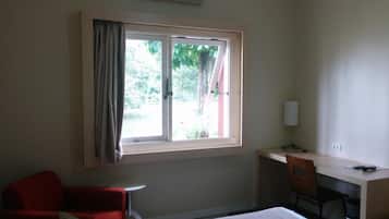 Quarto de hotel com cama, escrivaninha, cadeira e janela com cortinas.