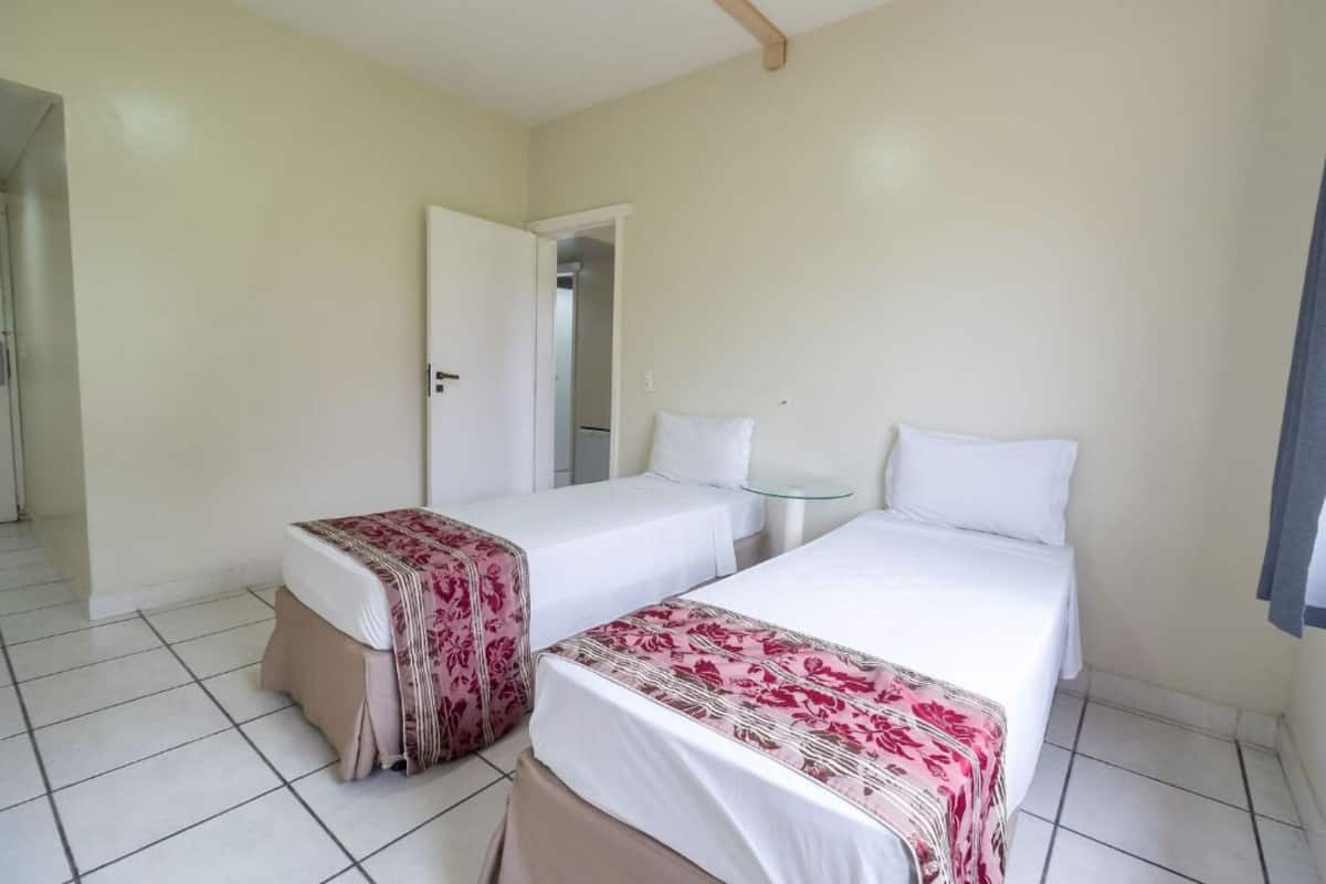 A room with two beds, a small table, and a door leading to another room.