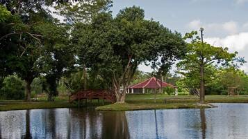 A serene park with a pond, a red bridge, and a building with a red roof.