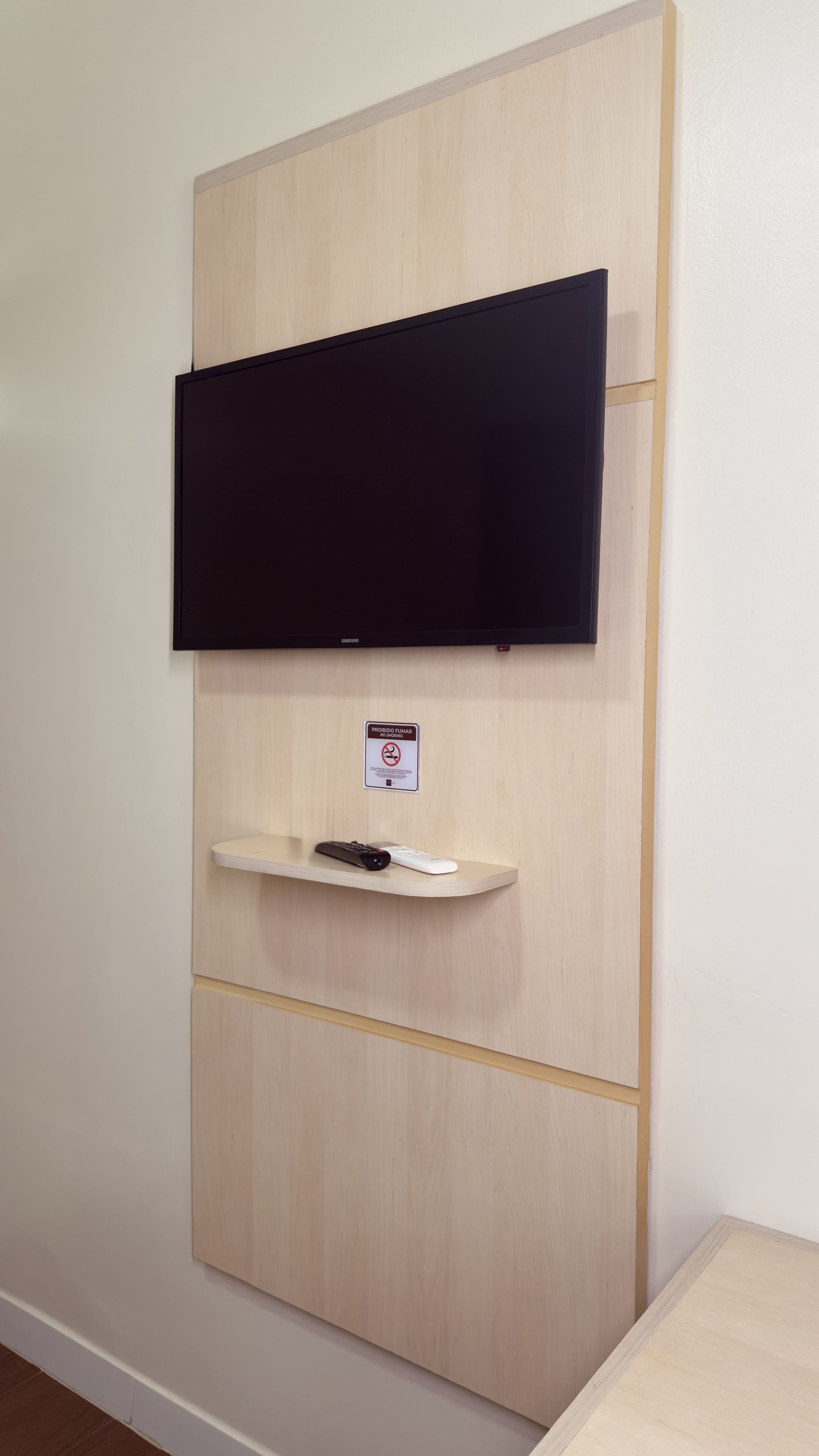 Un téléviseur fixé au mur, au-dessus d’une étagère, avec une télécommande.
