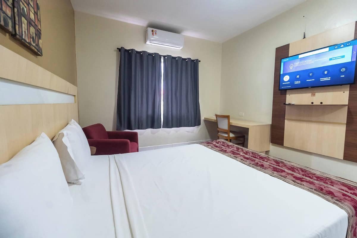 A hotel room with a bed, a desk, a chair, a TV, and a window with curtains.
