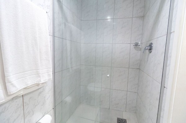 Un box de ducha con paredes de vidrio, azulejos de mármol blanco, un cabezal de ducha de mano y una toalla colgada en la pared.