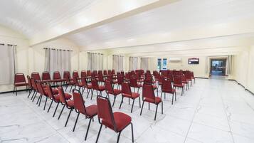 Un amplio salón de conferencias con filas de sillas rojas, suelo de mármol blanco y un techo alto.