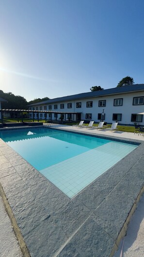 A swimming pool with a tiled deck, surrounded by lounge chairs and a building with multiple windows. - Nobile Hotel Belem (Belém)