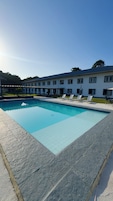 A swimming pool with a tiled deck, surrounded by lounge chairs and a building with multiple windows.