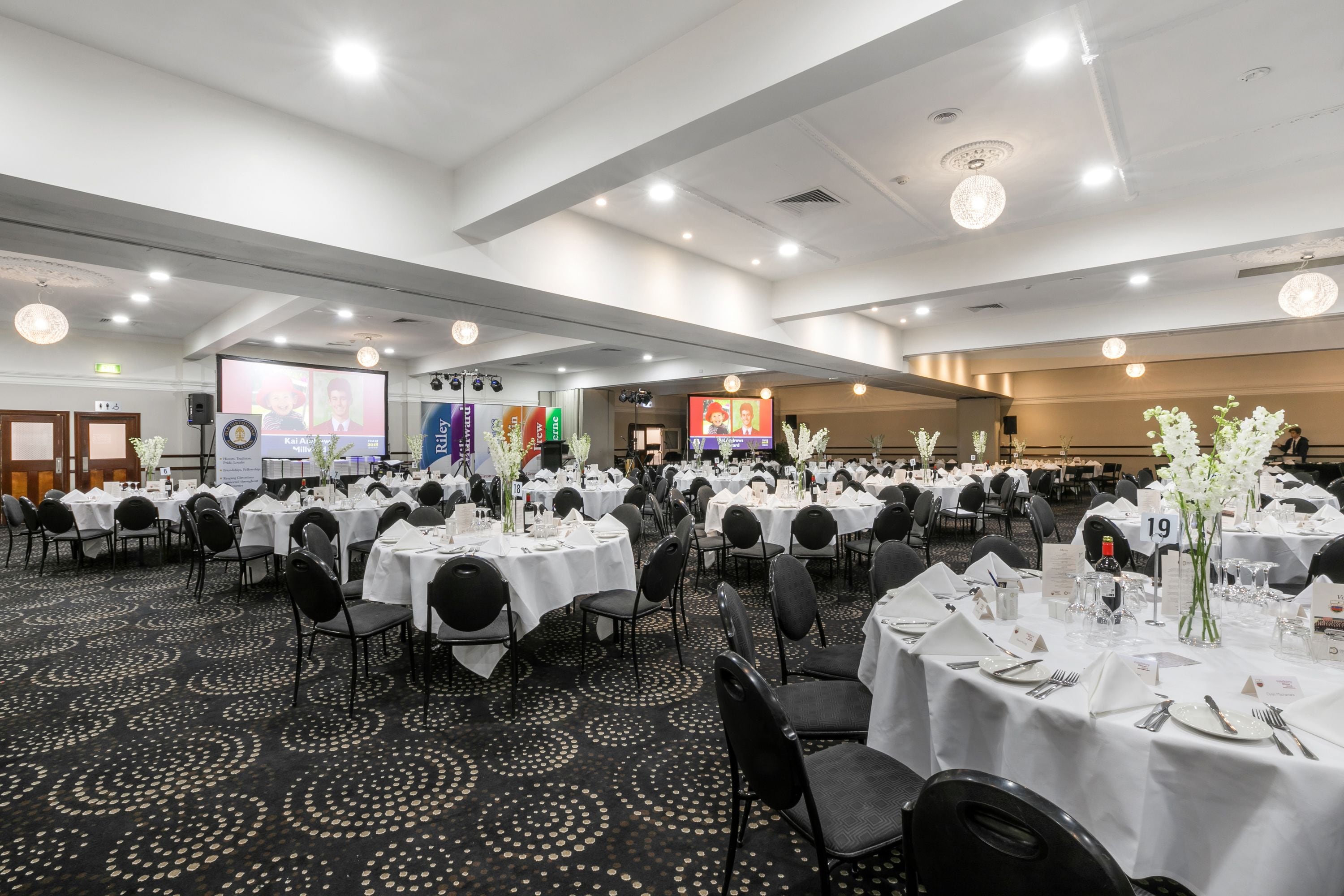 Un salón de banquetes con mesas redondas dispuestas para comer, equipado con sillas, vajilla y tarjetas de identificación numeradas.
