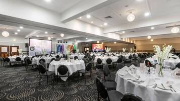 Un salón de banquetes con mesas redondas dispuestas para comer, equipado con sillas, vajilla y tarjetas de identificación numeradas.
