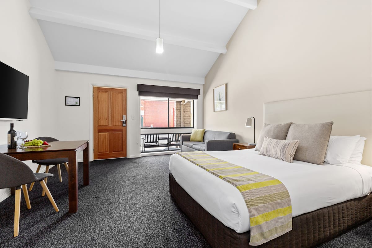 Quarto de hotel com uma cama, uma escrivaninha com cadeira, televisão e janela com vista para o exterior.