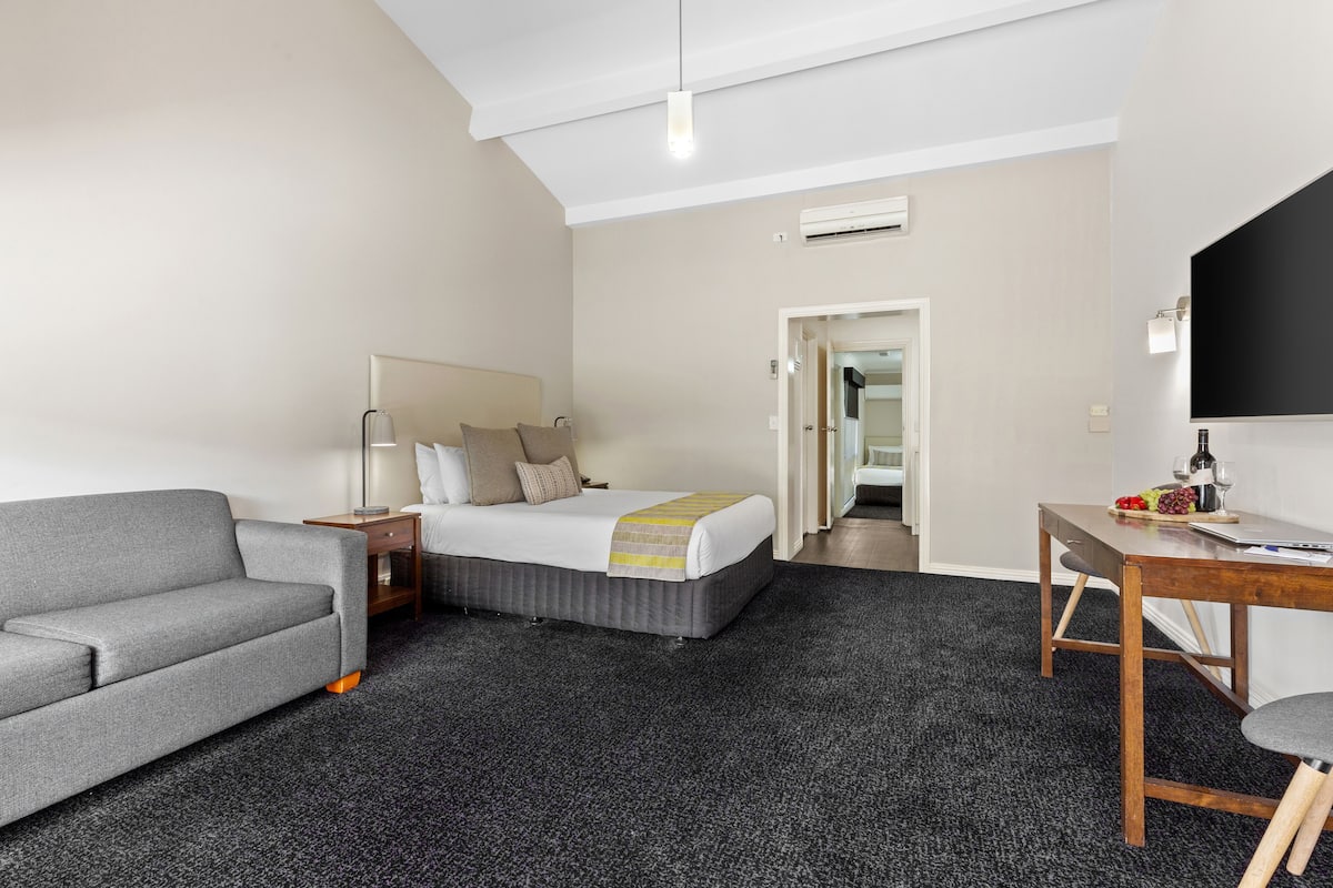Quarto de hotel moderno com uma cama, um sofá, uma escrivaninha e uma TV de tela plana.