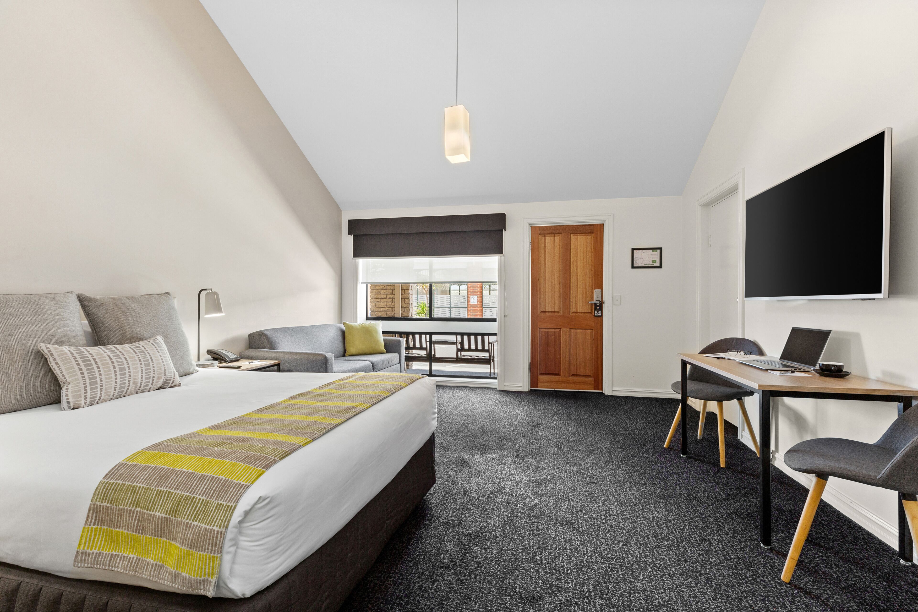 A hotel room with a bed, a desk, a chair, a TV, and a balcony with a view.