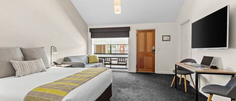 A hotel room with a bed, a desk, a chair, a TV, and a balcony with a view.