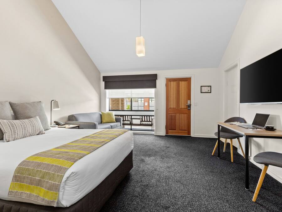 A hotel room with a bed, a desk, a chair, a TV, and a balcony with a view.