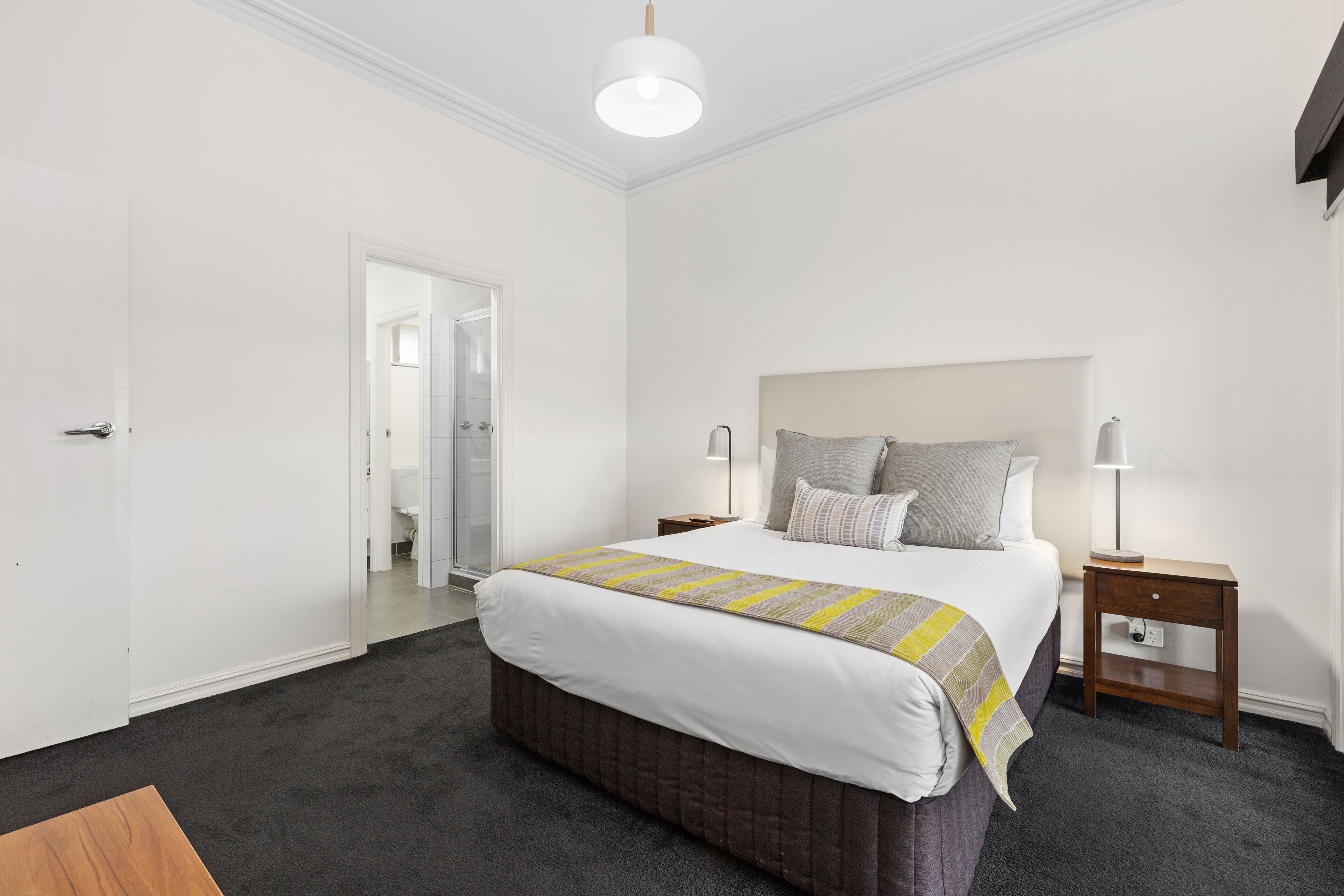 A bedroom with a large bed, a bedside table with a lamp, and a door leading to another room.
